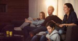 En familie som sitter i sofaen og smiler og ser på TV.